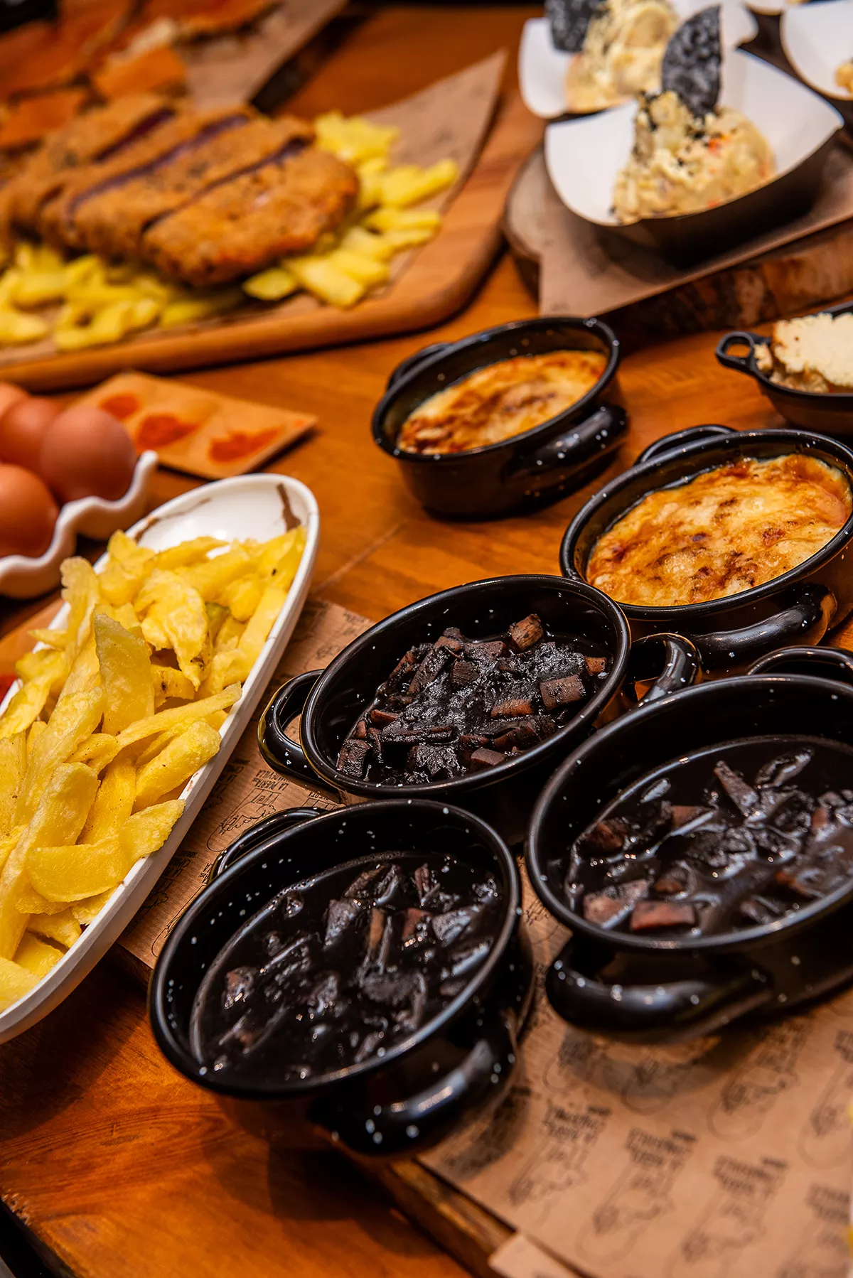 Bodegón con cazuelitas de calamares en su tinta, patatas fritas, cachopo, ensaladilla rusa y huevos cocidos