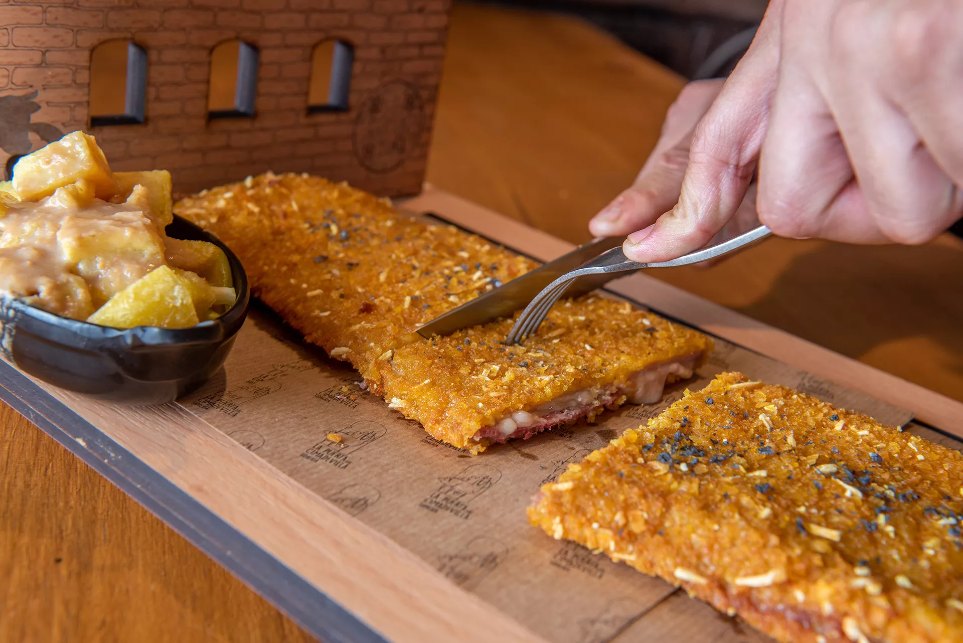 Mano cortando un cachopo con cuchillo y tenedor