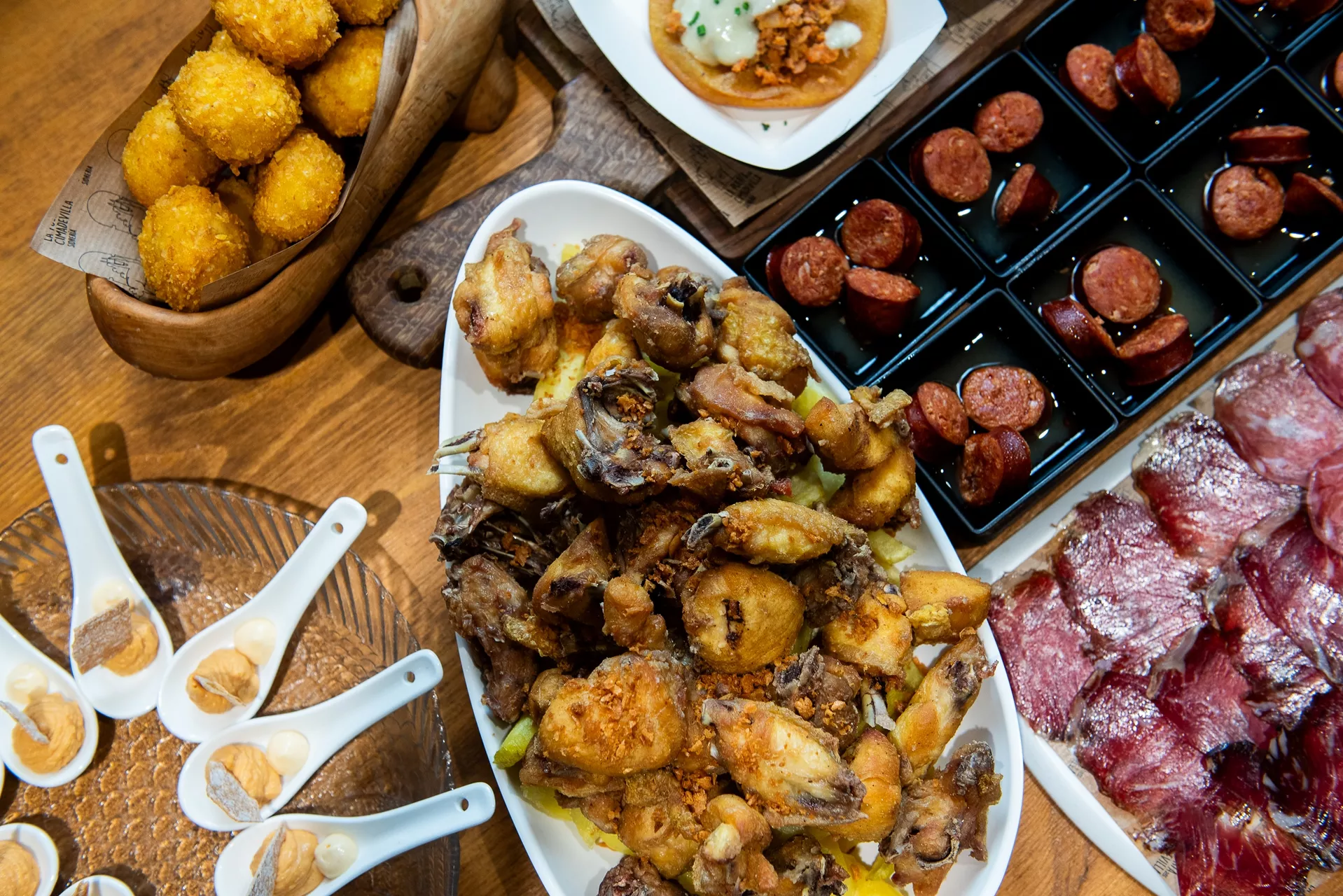 Bodegón con pollo frito, embutido, chorizo a la sidra, croquetas, tortos de picadillo y cucharitas de pastel de roca del Cantábrico con mahonesa de oricios