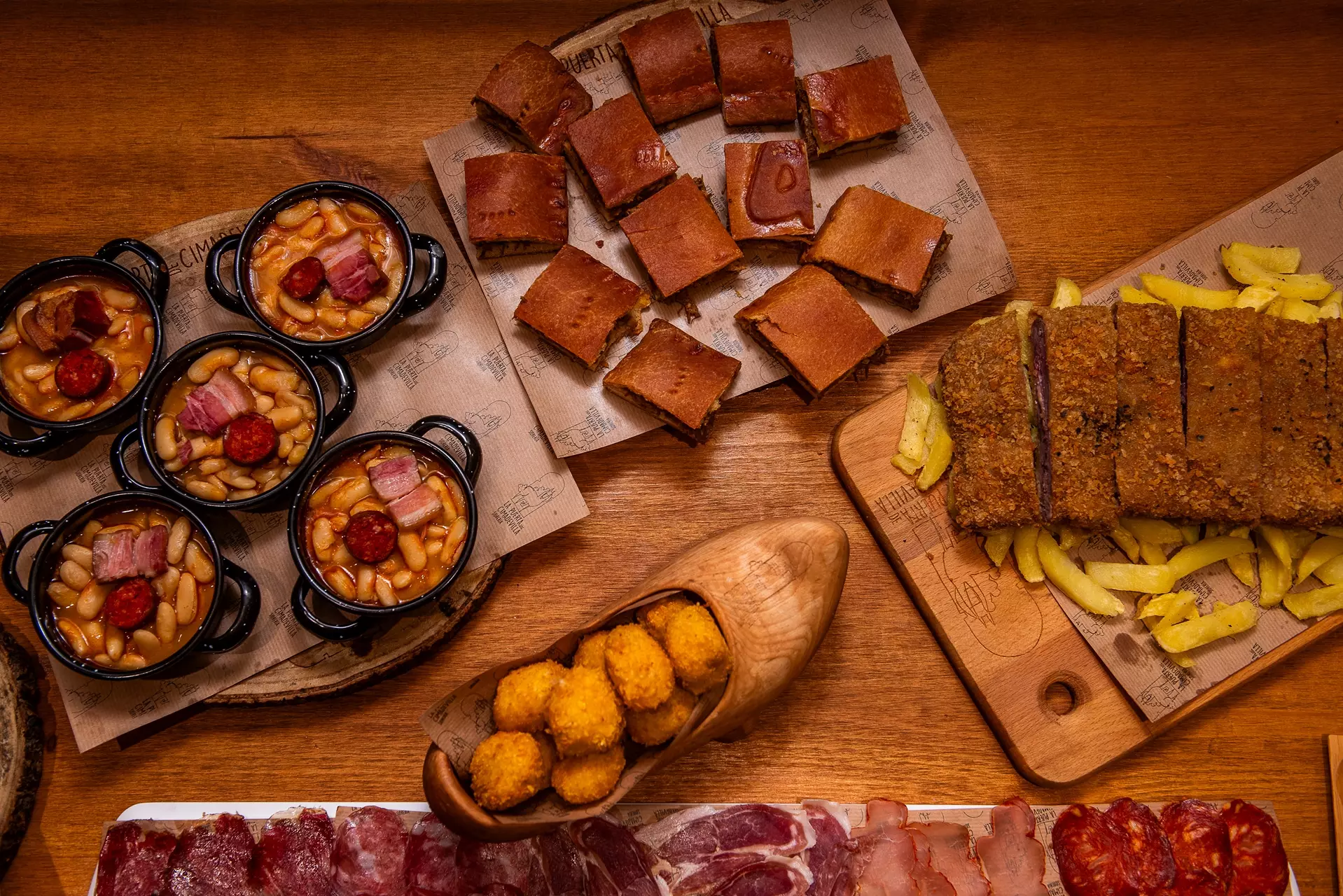 Bodegón con cazuelitas de fabada, empanada, cachopo, croquetas y embutidos